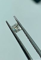 Diamond held in tweezers showing princess cut facets