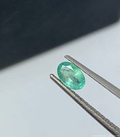 Oval cut emerald held by tweezers side view