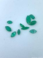 Group of ten marquise emeralds on white surface