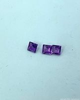 Three square (princess cut) amethyst gemstones on light surface