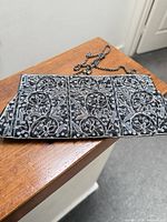 Front of black evening bag showing full silver embroidery and chain strap