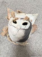 Front view of grey ceramic cat mask showing feather loss and overall appearance