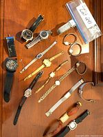 Overview of all sixteen wristwatches arranged on wood surface