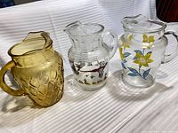 All three pitchers side by side: amber textured, clear with pheasants, clear with floral decal