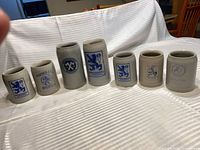 Seven stoneware beer steins lined up on cloth