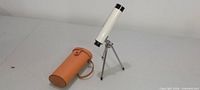 Telescope mounted on tripod beside tan carrying case