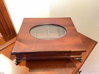 Closed hardwood jewelry box showing oval glass window and metal feet