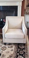 Front view of beige linen-like accent armchair showing nailhead trim, seat cushion and legs