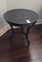 Full view of round black wood accent table on hardwood floor