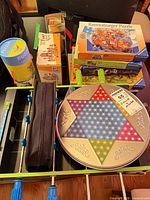 Lot overview with foosball table, Chinese Checkers tin, cylindrical puzzle, and stack of boxes