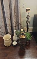 Group shot of all items against drapery: metal vase, ceramic vases, planter, pitcher, faux plant, candle and iron stand