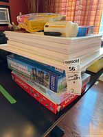 Stack showing canvases, Monopoly games, Structural Engineering kit, packaged Play-Doh set, small handheld items