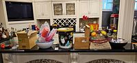 Wide view of countertop showing entire assortment: cake stand, holiday tin, disposable cups, utensil holder, boxes