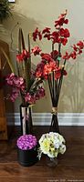 Group shot of all four decorative pieces: red orchid bundle, silver vase with orchids, hatbox of roses, glass compote arrangement
