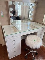 Front view of vanity showing glass top, mirror with bulbs, drawer layout, stool