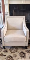 Front view of beige upholstered armchair with nailhead trim and removable cushion