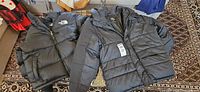 Two black puffer jackets laid flat; North Face on left, Zoo York on right