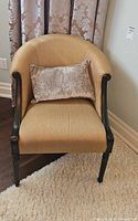 Front view of gold upholstered barrel armchair with pillow