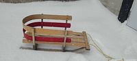 Side view of wooden sled in snow showing red side slats and pull rope