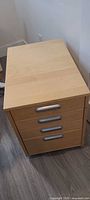 Front view of light wood four-drawer filing cabinet showing handles and casters