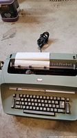 Front view of IBM Selectric typewriter with paper loaded and power cord visible