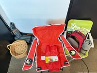 Red folding chair, green chair, picnic backpack, rolled blanket, basket, pole bag visible