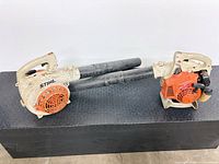 Two Stihl gas leaf blowers side by side with blower tubes attached