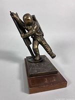 Front three-quarter view of brass astronaut figure on wood base