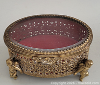 overall view of oval metal filigree jewelry box, glass top, red lining