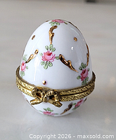 Front angle of porcelain egg trinket box showing floral design and metal hinge