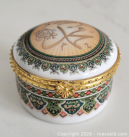 Angled view of porcelain trinket box showing gold-tone clasp and decorative band