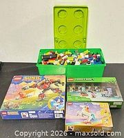Green bin filled with assorted Lego bricks and three boxed Lego sets displayed
