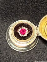 Top view of ring in a display showing red center stone with halo of clear stones