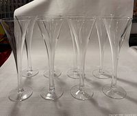 Front view of eight clear glass trumpet champagne flutes standing upright