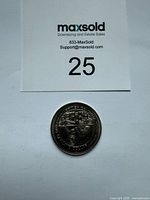 Coin with MaxSold lot card for scale
