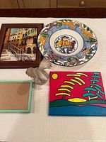 Group shot showing all five items: painting, ceramic plate, eagle figurine, two picture frames