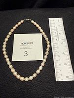 Strand of pearls arranged beside ruler on black surface