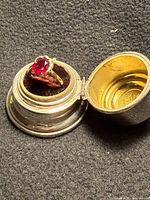 Ring in closed circular case showing red stone and gold band