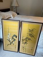Both framed silk screens leaning against bed