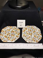 Front view of both octagonal floral plates with ruler for scale