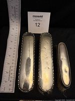Three sterling silver clothes brushes next to ruler for scale