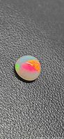 Round cabochon opal showing multicolour play-of-color on black textured background