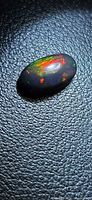 Front view of oval black opal showing multicolour flashes