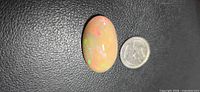 Oval opal cabochon beside a coin for scale