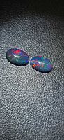 Two oval black opals on textured dark surface showing multicolor flashes