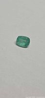Top view of loose cushion-cut emerald on neutral background