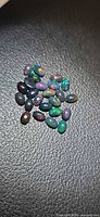 Group of small oval black opal cabochons on textured background
