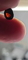 Front view of oval cut deep orange tourmaline held between fingers