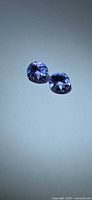 Two violet-blue faceted gemstones on neutral background