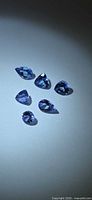 Six loose violet-blue Tanzanite stones on light background